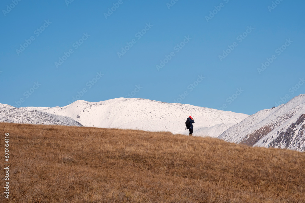 Back of girl while climbing on the top of mountain. Woman photographer with a backpack walking on snow. Blue sky. Copy space.