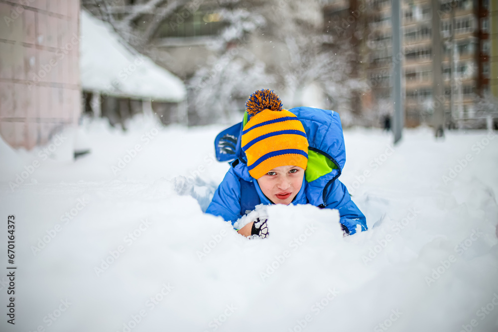 Cute little boy having fun with snow in winter park. Happy child playing with snow in winter park