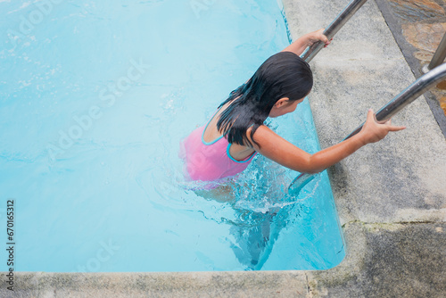 Girl in a pink swimsuit climbing the pool ladder. photo