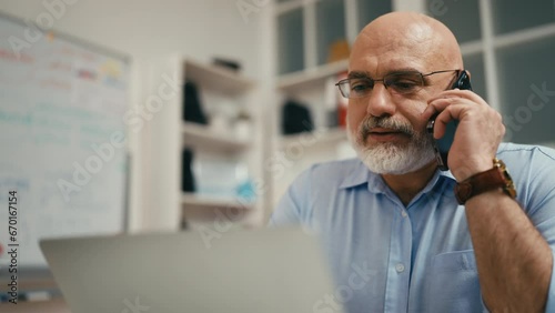 Middle-aged man talking on phone in his office, successful businessman concept