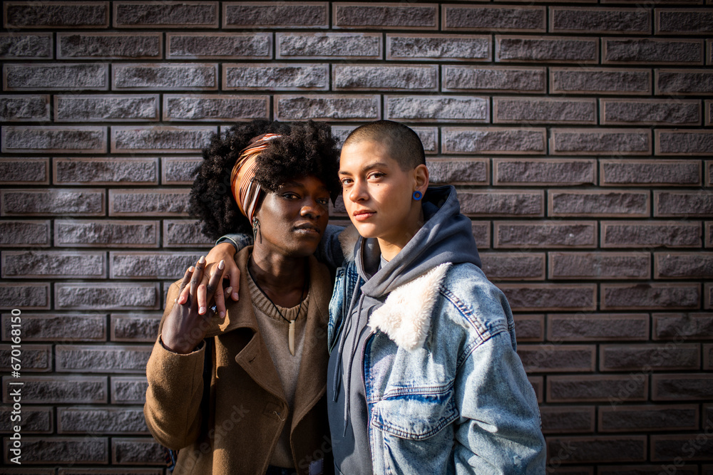 © Marko Geber - Portrait of lesbian couple hugging each other with a brick wall background