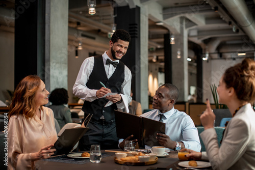 Attentive Waiter Assisting Guests with Menu Choices in Hotel Restaurant photo