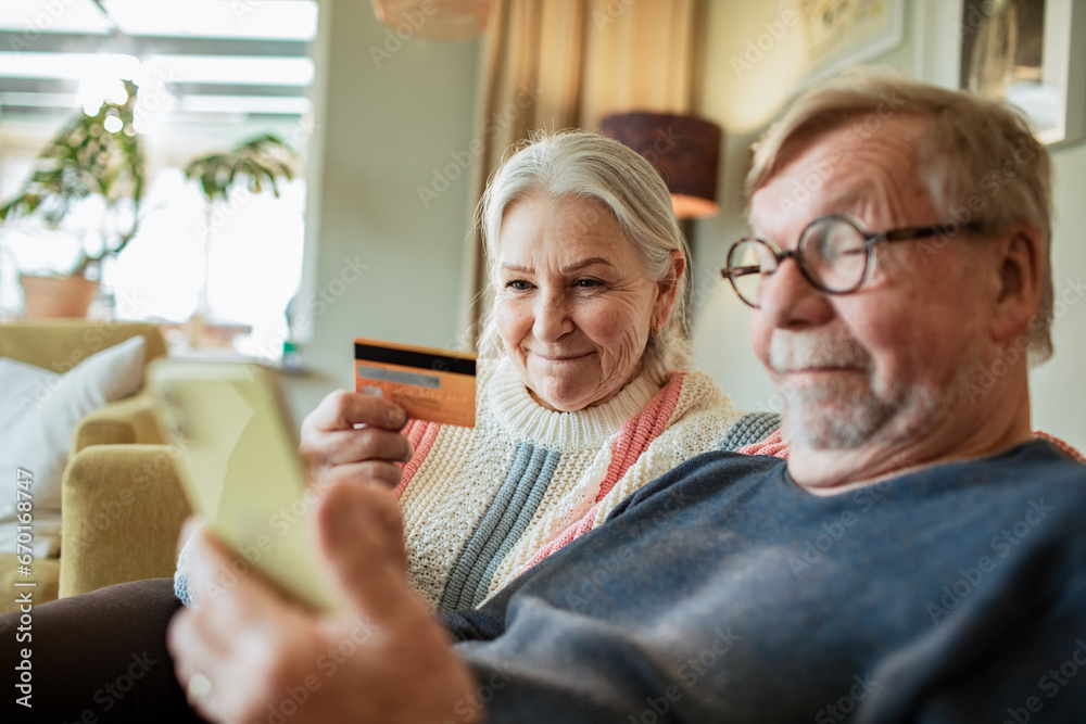 Senior Caucasian couple online shopping from a smartphone on the couch at home