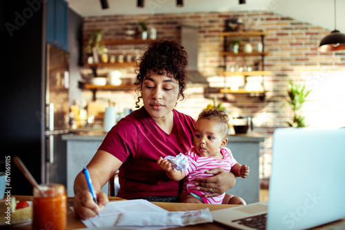 Focused mother multitasking between work and baby in a cozy kitchen photo