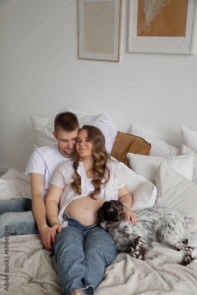 Couple in love, pregnant girl and guy with dogs on bed, bright photo Couple in love, pregnant girl and guy with dogs on bed, bright photo