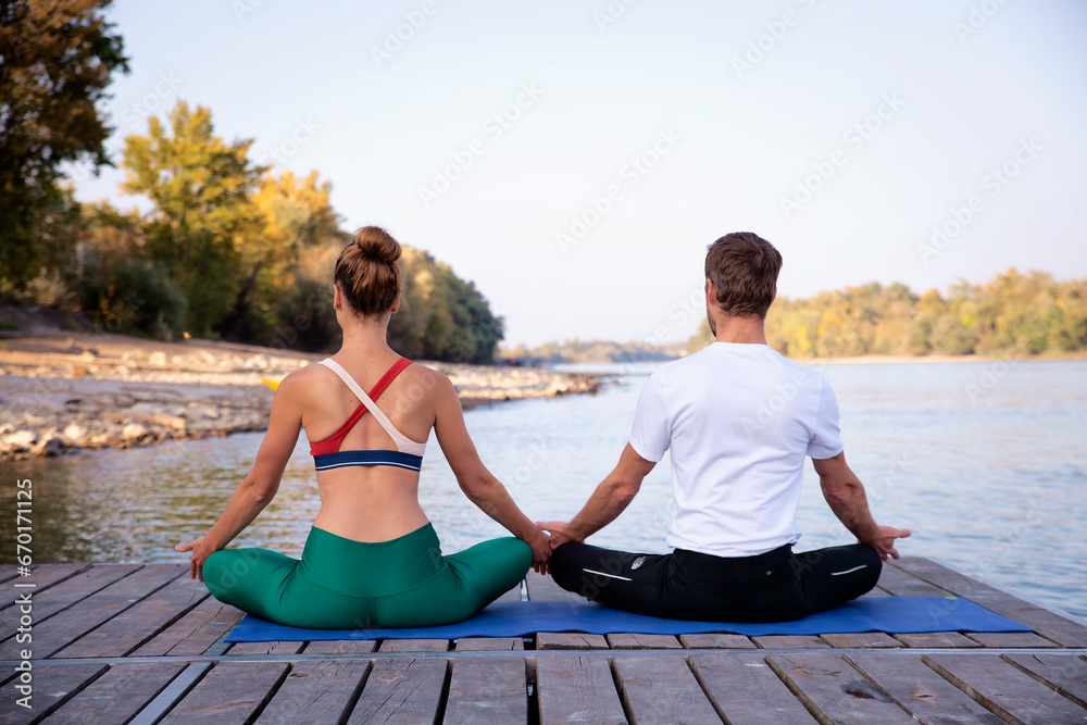 Rear view of a woman and a man sitting in lotus position on yoga mat outdoor and meditating