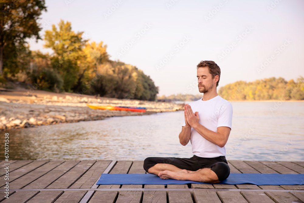 Full length of caucasian man practicing yoga on pier by lake