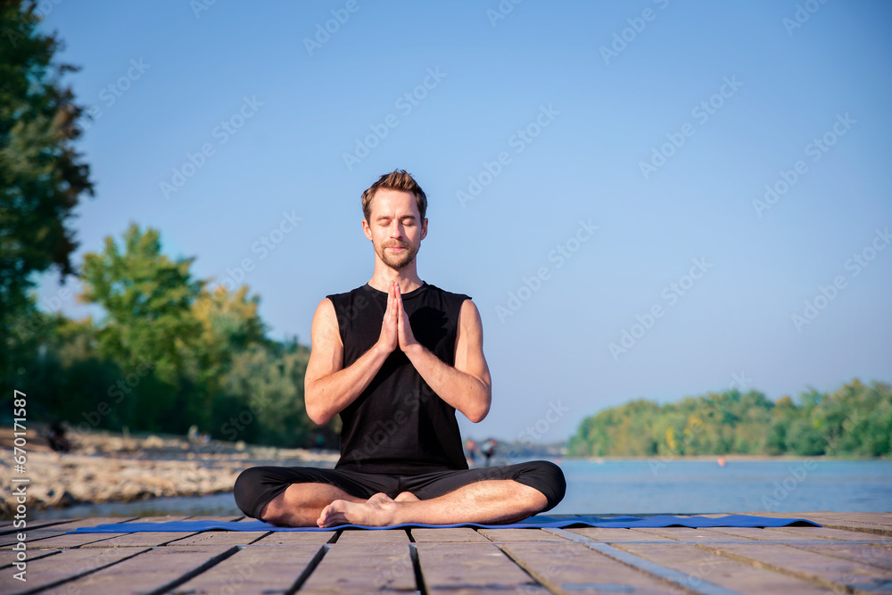 Mature man doing yoga exercise on jetty against blue sky