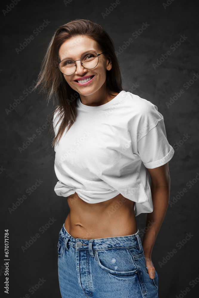 Radiant female in glasses and a white cropped tee proudly displays her toned core on a dark setting Radiant female in glasses and a white cropped tee proudly displays her toned core on a dark setting