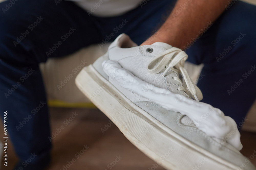 Cleaning suede sneakers. A worker in a shoe workshop cleans a pile of shoes - obrazy, fototapety, plakaty 