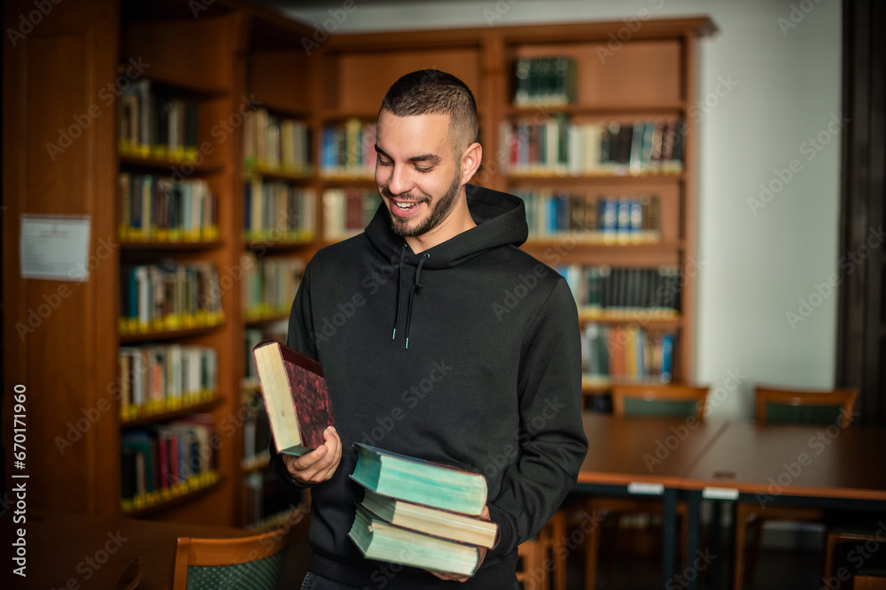 Young man standing in the university library and holding books in his hand Young man standing in the university library and holding books in his hand