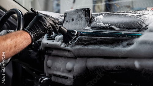 A mechanic cleans the interior of a car with a brush and foam.
