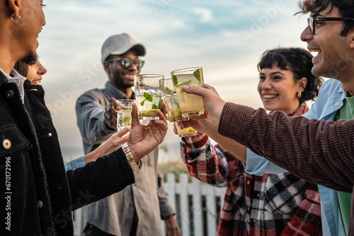 Quadro su tela Cheerful friends with summer drinks - Joyful group of friends raising glasses filled with refreshing drinks, toasting to a good time outdoors with a clear sky backdrop