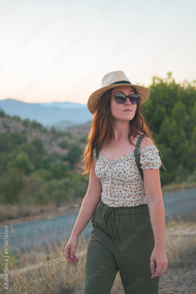 Portrait of a woman walking in the countryside wearing a straw hat and sunglasses