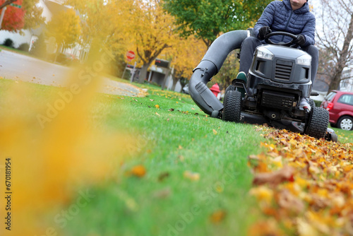 Mowing the grass with a lawn  tractor mower in sunny autumn. Gardener cuts the lawn in the garden