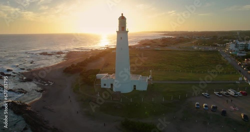 Aerial shot from a drone, open plan, of the Lighthouse located in Uruguay on a clear day. This lighthouse is located in the town of La Paloma. The sun is setting behind. It's a short shot of the light