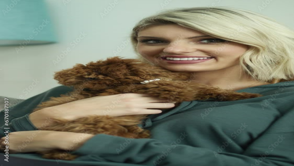 Portrait of smiling woman sitting on sofa hugging dog  - vertical video / Vineyard, Utah, United States