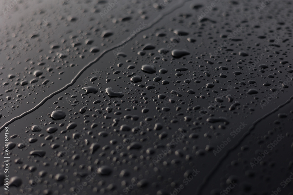 Rain or water drops different size on a black shiny car hood surface. Water droplets on dark iron surface and texture. Abstract background and water texture for design.