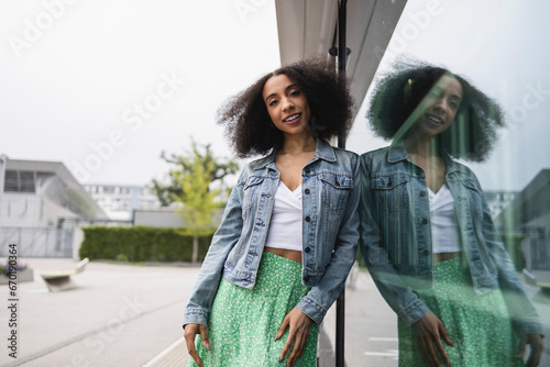 Ethnic young woman smiling and leaning against a reflective glass pane photo
