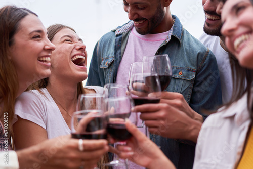 Close up photo of mixed race group of friends having fun, laughing, talking, and toasting with red wine. Happy people gathered enjoying the good times.