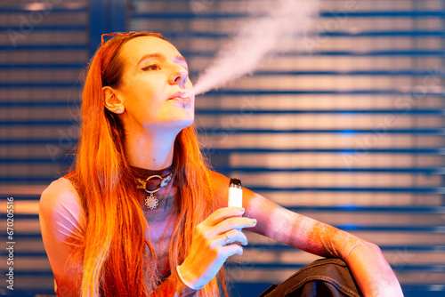 Young woman vapor exhales near blue metallic backdrop photo