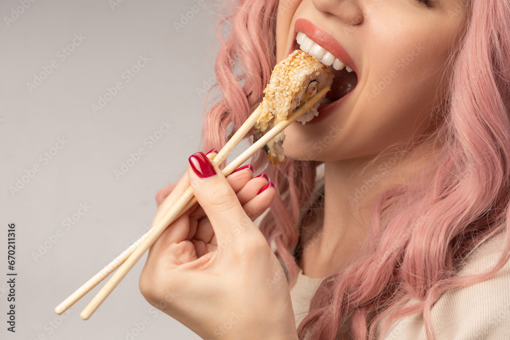 Young woman with red nails and pink hair is eating sushi. Young woman with red nails and pink hair is eating sushi.