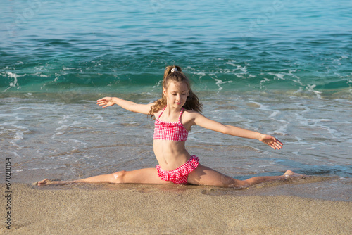 Pretty little girl in red swimming suit doing splits on the beach.