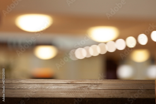 Empty wooden tabletop on light golden bokeh of a cafe restaurant on a dark background