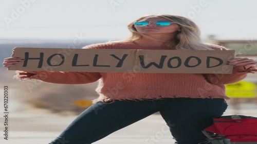 Woman holding Hollywood sign hitchhiking on remote rural road  - vertical video / Loa, Utah, United States