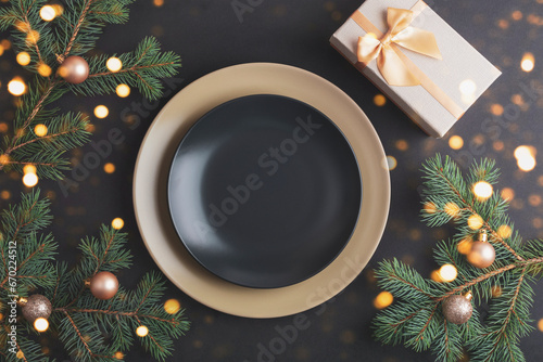 Stylish table setting with fir branches and Christmas balls, black plate and gift box on black background. Christmas concept. Top view, flat lay