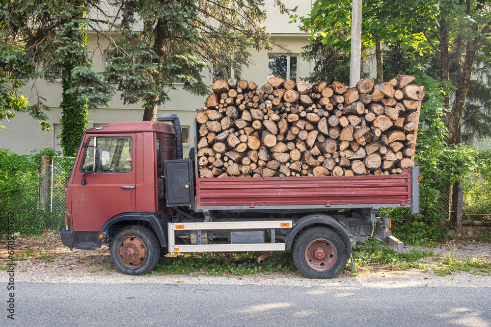 Dump truck with a body full of firewood. Truck loaded with stack of wooden logs to delivery for heating season. Firewood for the stove during the winter cold