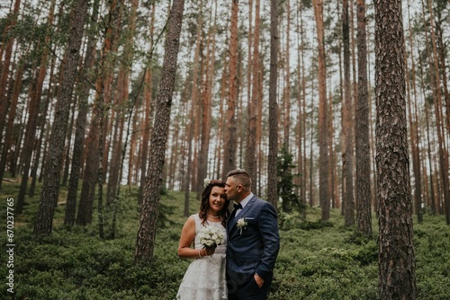 bride and groom in forest pine trees. The groom kisses the bride's forehead.
