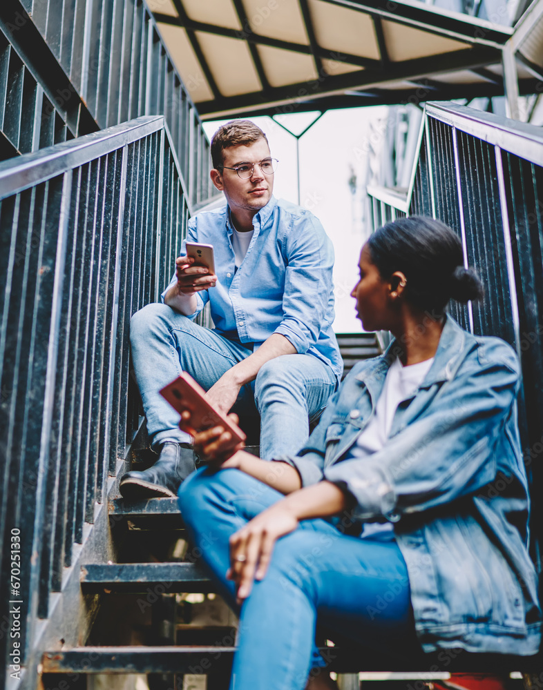 Multicultural young man and woman with mobile phones sitting on stairs of house Multicultural young man and woman with mobile phones sitting on stairs of house