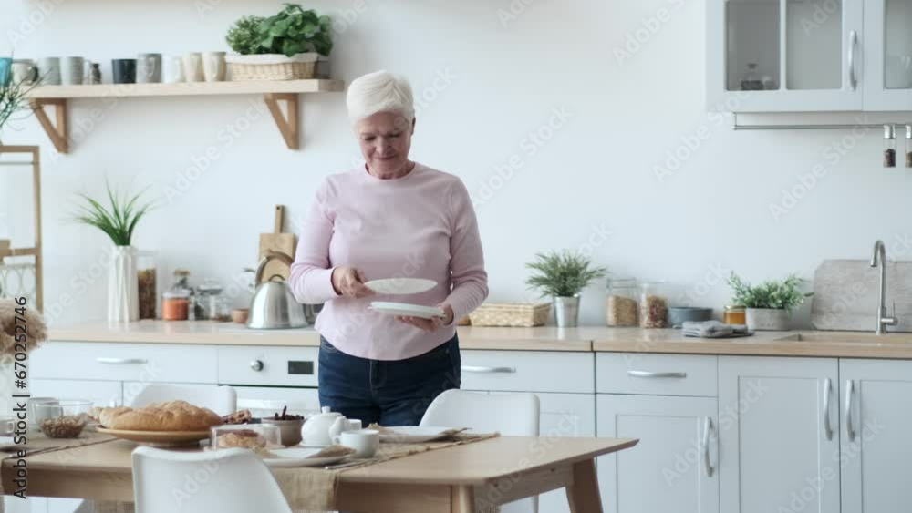 Nurturing Caucasian woman arranges plates on the table in the kitchen. Her hands move with purpose and gentleness, ensuring each plate finds its place with precision. Nurturing Caucasian woman arranges plates on the table in the kitchen. Her hands move with purpose and gentleness, ensuring each plate finds its place with precision.
