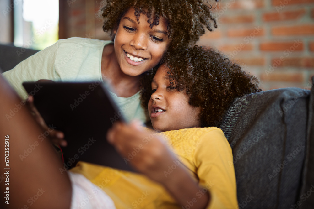 Little African American kids relaxing on sofa at home and watching something on digital tablet