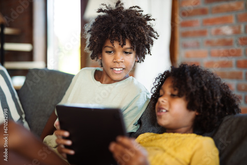 Little African American kids relaxing on sofa at home and watching something on digital tablet