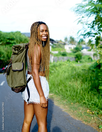 positive dark skinned traveller with backpack standing on road enjoying weekends