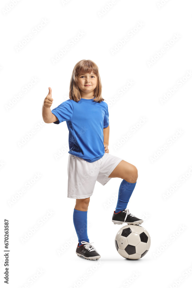 Girl in sports jersey standing with foot on top of a football and gesturing thumbs up
