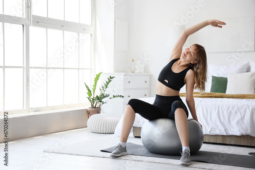 Young sporty woman stretching with fitness ball during training at home