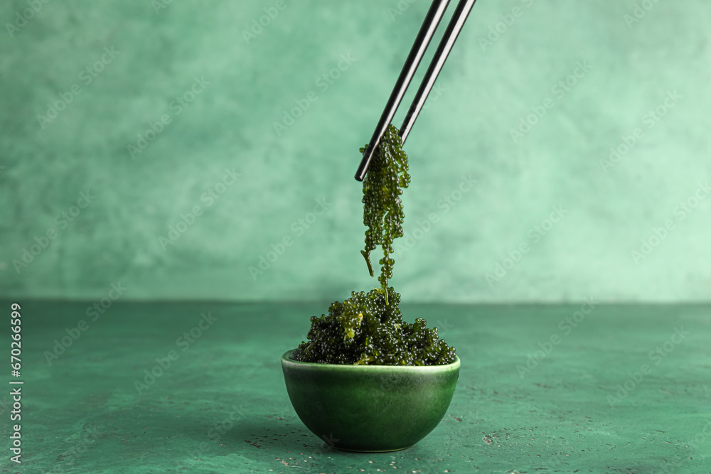 Bowl and chopsticks with healthy seaweed on green background - obrazy, fototapety, plakaty 
