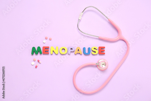 Word MENOPAUSE with pills and stethoscope on pink background