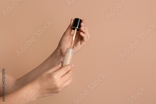 Female hands with bottle of liquid makeup foundation on color background, closeup