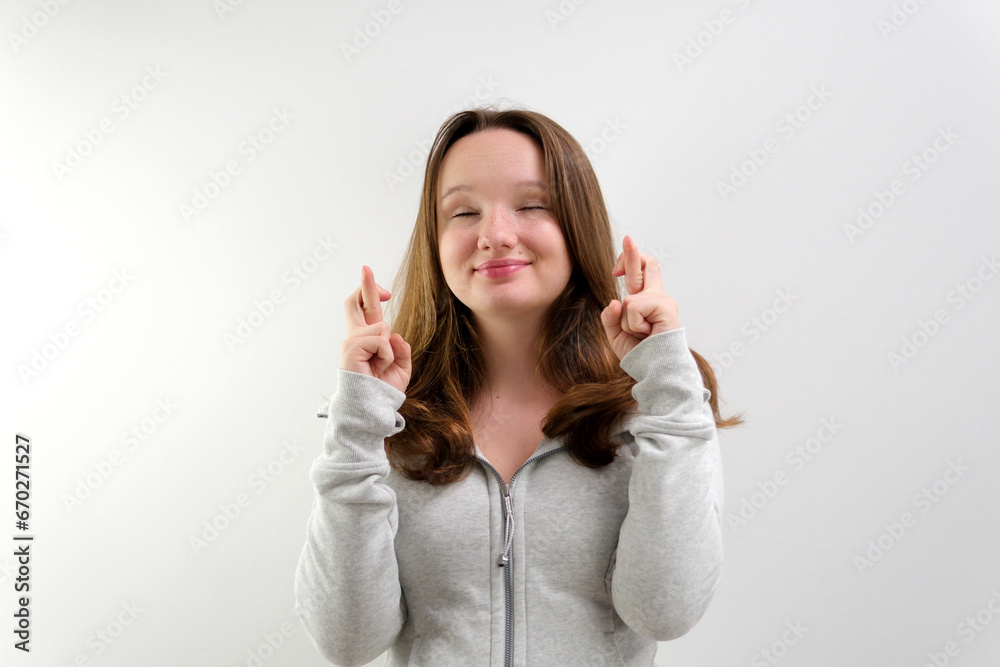 Intrigued woman in t-shirt praying with crossed fingers and looking away over grey background. High quality photo Intrigued woman in t-shirt praying with crossed fingers and looking away over grey background. High quality photo