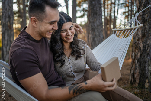 Young couple man and woman give present gift box while sit in nature