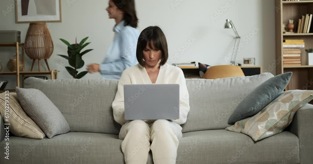 Focused mother diligently works on laptop while children play energetically around. Her ability to maintain concentration amidst the lively activity showcases multitasking skills. Focused mother diligently works on laptop while children play energetically around. Her ability to maintain concentration amidst the lively activity showcases multitasking skills.