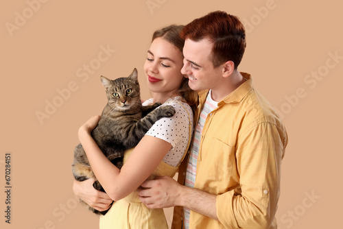 Young couple with cute cat on beige background