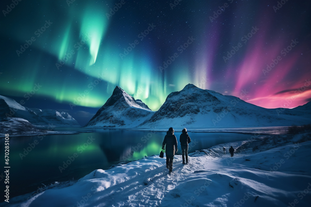 A distant photo of a group of tourist mountaineers and their guide are hiking to a rock in front of a mountain lake with thick coats on a in snow covered mountain hill with northern lights with trails - obrazy, fototapety, plakaty 