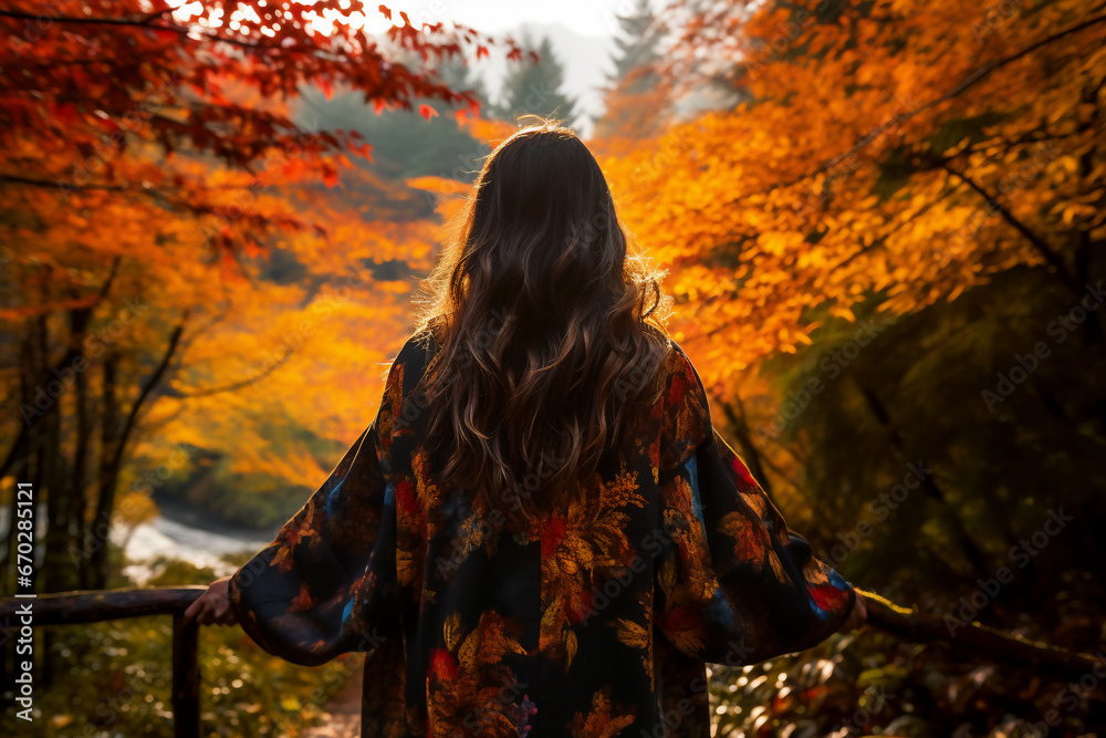 A young asian woman is posing in front of the camera from the front happily with an autumn coat in a forest during sunset in autumn in a vibrant coloration - obrazy, fototapety, plakaty 