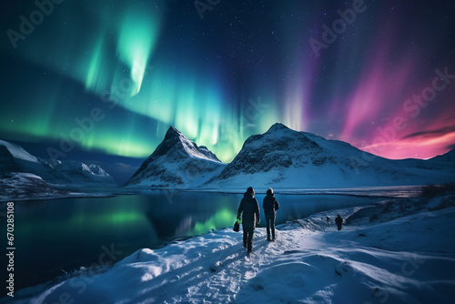 A distant photo of a group of tourist mountaineers and their guide are hiking to a rock in front of a mountain lake with thick coats on a in snow covered mountain hill with northern lights with trails