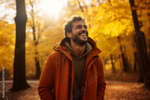 A young latin man is walking happily with an autumn coat in a forest during sunset in autumn with a vibrant coloration
